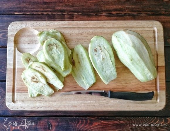 Сначала необходимо заняться баклажанами. Их необходимо очистить от кожуры, очень удобно это делать овощечисткой. Затем острым ножом я нарезала баклажаны на полоски толщиной 3–5 мм. Толще делать не стоит, в противном случае увеличится время на готовку в духовке, и сыр приобретет не красивую золотистую корочку, а станет коричневым и жестковатым. Поэтому не торопимся и делаем тоненькие полоски.