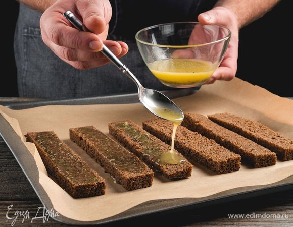 Полейте чесночным маслом с травами кусочки хлеба и выложите на противень с пергаментной бумагой.