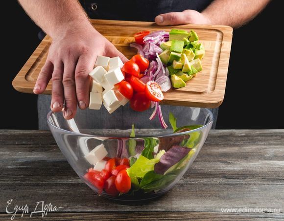 Порвите салатные листья руками и застелите блюдо. Выложите горкой вперемешку авокадо, фету, томаты и красный лук.
