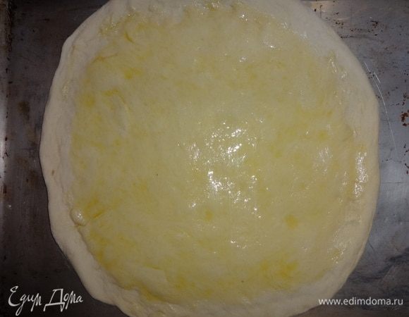 Выложить основу для пиццы на противень, смазанный растительным маслом. Смазать круг теста оливковым масло, не доходя до краев 1–1,5 см.