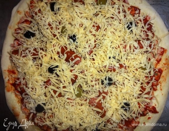 Сыр натереть на крупной терке. Посыпать начинку сыром. Поставить пиццу в духовку, разогретую до 180°C, на 20–25 минут.
