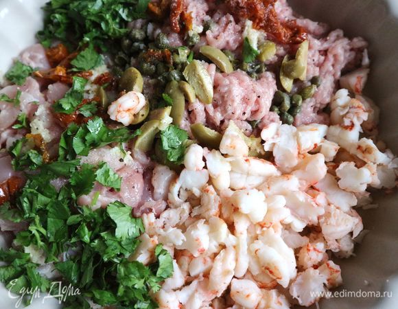 Духовку разогреть до 180°C. Креветки на пару минут опустить в кипящую воду, откинуть на дуршлаг, чтобы обсохли. Смешать кусочки куриных бедер, фарш, нарезанные крупно и остывшие полностью креветки, нарезанную зелень, оливки, каперсы, добавить сухое белое вино, оливковое масло, соль (чуть-чуть, ведь в смеси есть соленые ингредиенты).