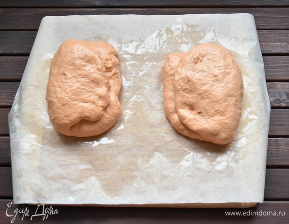 Поле того, как тесто увеличится в объеме, разделить его на две части. Каждую часть свернуть дважды конвертом, выложить на промасленную пергаментную бумагу и оставить еще на 30 минут.