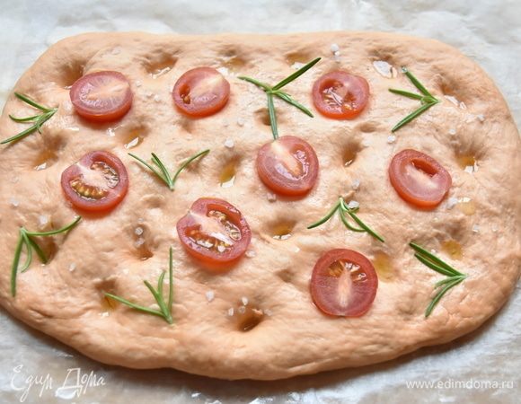 Через 30 минут разровнять тесто руками, придав ему форму лепешки. Пальцами сделать в лепешке углубления, сбрызнуть небольшим количеством оливкового масла. Можно вдавить в тесто половинки помидоров черри, молодые веточки розмарина или оливки. Сверху посыпать гранулами морской соли.