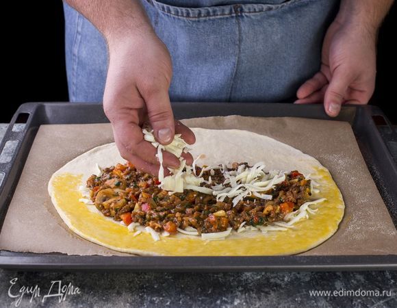 Раскатайте пласт теста, смажьте его по краю яйцом, смешанным с оливковым маслом. Посыпьте тесто тертой моцарелой. Выложите на одну сторону фарш, сверху добавьте еще немного моцареллы.