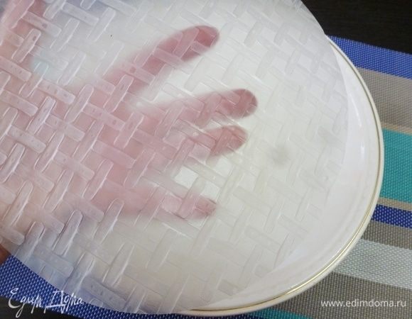 В широкую тарелку налить кипяченную теплую воду. Опустить в нее листы рисовой бумаги на несколько (буквально на 5–7) секунд. Учтите, чем теплее вода, тем быстрее размокает бумага. Не размачивайте рисовую бумагу совсем, пусть она будет немного жестковата, потом она дойдет на доске. Сильно размоченный лист может порваться или слипнуться. Мне нравится заворачивать спринг-роллы на мокрой деревянной доске. Дерево хорошо смачивается и хорошо впитывает влагу.