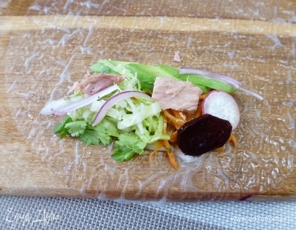 Итак, на мокрую деревянную доску раскладываем мокрый рисовый блинчик. На блинчик кладем всего понемногу из приготовленных продуктов: пекинскую капусту, свежий огурец, красный лук, авокадо, острую морковку, вареную свеклу, редиску, консервированный тунец ТМ «Магуро», зелень кинзы и петрушки.