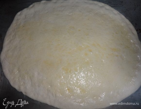 Дрожжевое тесто ( которое я готовила в рецепте «Пицца „Тарантелла“») раскатать в тонкий пласт. Сегодня мне захотелось сделать пиццу в форме овала. Смазать поверхность теста оставшимся оливковым маслом, не доходя до краев 1–1,5 см. Выложить тесто на противень, смазанный растительным маслом.