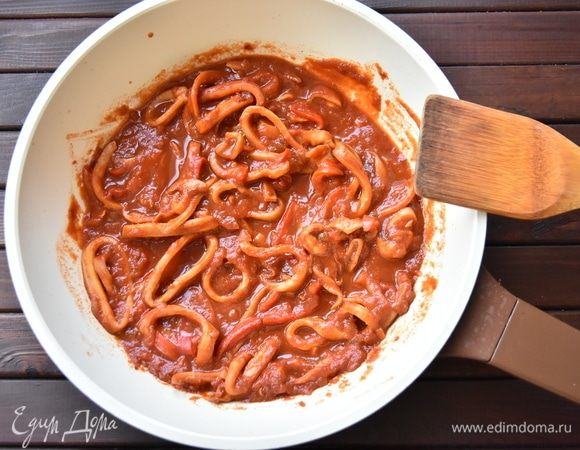 К овощам выложить томаты в собственном соку. Предварительно помидоры можно нарезать, размять вилкой или пюрировать погружным блендером. Потушить овощную смесь минут 10 до желаемой густоты. Соус посолить, по вкусу добавить сахар. Выложить подготовленных кальмаров и тушить еще 5–7 минут.