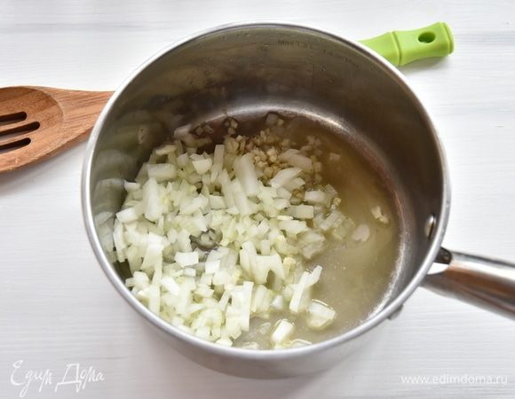 В сотейнике разогреть сливочное и оливковое масла, выложить лук и чеснок. Потомить овощи на медленном огне минуты 3.
