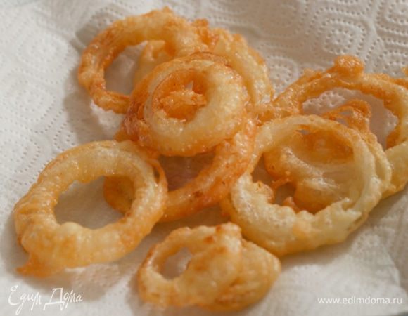 Луковые кольца обмакивать в кляр и жарить во фритюре до золотистого цвета, затем выкладывать на бумажное полотенце.