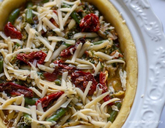 Сверху разложить вяленые томаты и слегка посыпать натертым сыром. Отправить в разогретую до 180°C духовку выпекать 30–35 минут.