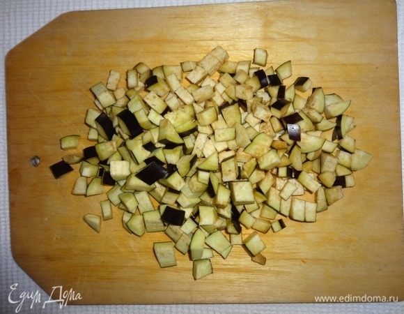 Баклажаны помыть, вытереть бумажным полотенцем. Отрезать плодоножки. Нарезать баклажаны небольшими кубиками. Добавить баклажаны в сковороду и продолжать обжаривать овощи, помешивая.
