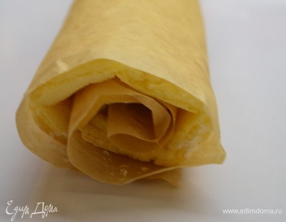 Вытащить готовый бисквит и перевернуть на бумагу, припыленную кукурузным крахмалом. Бумагу, на которой выпекался бисквит, аккуратно снять. Свернуть бисквит в рулет прямо с бумагой и оставить остывать.