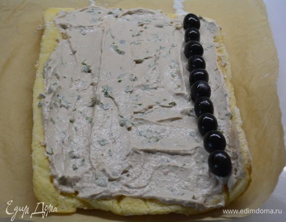 Развернуть рулет и смазать равномерно его начинкой из печени и сыра. По краю выложить маслины в один ряд.