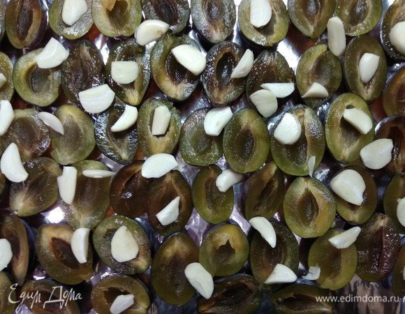 Сливы моем, обсушиваем, разрезаем пополам, удаляем косточку и укладываем на застеленный противень срезом вверх. Сверху кладем очищенные и разрезанные пополам зубчики чеснока.