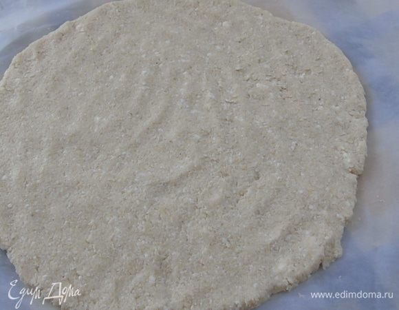 Выложите массу на пергамент и руками разровняйте в круг. Пицца должна быть тонкой. Примерно 0,5 см.