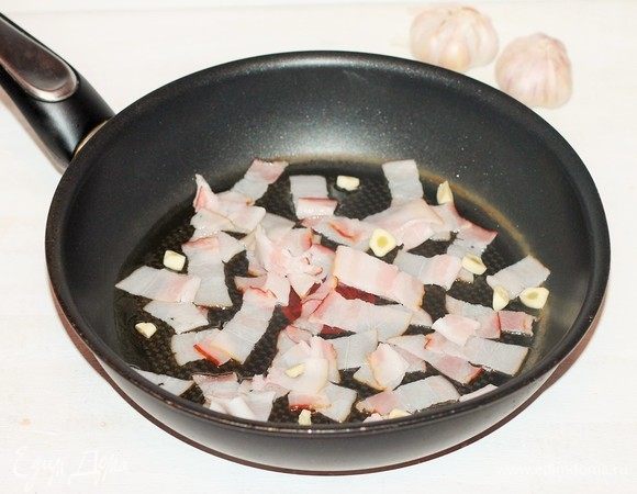 В большой сковороде разогреть масло, выложить нарезанный бекон (4 пластины) и очищенный порубленный чеснок, жарить, помешивая, около 2 минут.