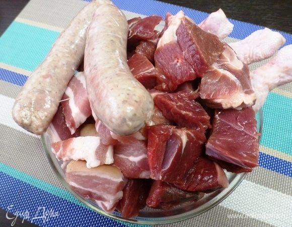 Все виды мяса берем примерно в одинаковых пропорциях. Нарезать все не слишком мелкими кусочками. Куриные голени я оставила как есть. А колбаски нужно разрезать острым ножом на 3–5 частей в зависимости от размера.