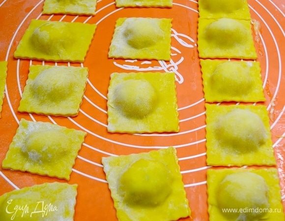 Далее начинку выкладываем на раскатанный пласт теста горками, смазываем промежутки желтком или водой с помощью кисточки, накрываем другим пластом теста и формируем равиоли, по краям проходимся вилкой или специальным кругом. Форма у равиоли может быть совершенно разной: квадратной, круглой, треугольной и т. д.