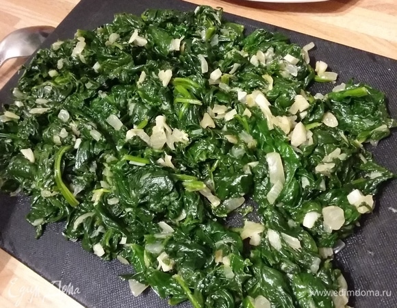 На разогретом оливковом масле пассеровать мелконарезанные лук и чеснок до прозрачности. Добавить вымытый и обсушенный шпинат и обжарить в течение нескольких минут, пока шпинат не «осядет». Остудить. Отжать жидкость, выложив его в сито и слегка прижав ложкой. Можно использовать размороженный шпинат, предварительно отжав из него жидкость. Выложить остывший шпинат на тарелку и мелко нарезать.