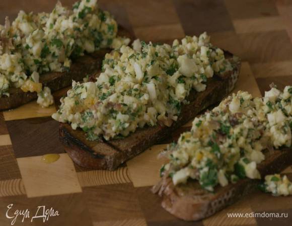 Второй зубчик чеснока разрезать пополам и натереть обжаренный хлеб, затем сбрызнуть оливковым маслом Extra Virgin и выложить на брускетту яичную начинку.