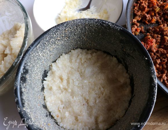 Духовку разогреть до 190°C. Неразъемную форму смазать сливочным маслом (5 г), посыпать панировочными сухарями. Положить на дно формы слой риса в палец толщиной.