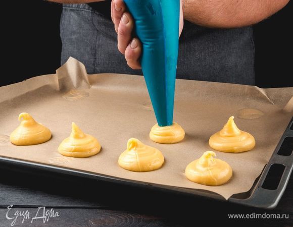 На застеленный пергаментом противень с помощью пекарского мешка выложите тесто в виде небольших профитролей. Выпекайте в разогретой до 190°C духовке в течение 15 минут. Затем уменьшите температуру до 170°C и выпекайте еще 15–20 минут. После выключения духовки оставьте готовые профитроли в ней минут на 10.