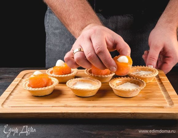 На тарталетку выложите сливочный сыр, в середину поставьте перепелиное яйцо, обернутое полоской лосося.