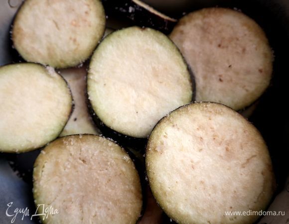 Каждый кружочек баклажана слегка натереть солью ( 40 г морской соли). Положить на дуршлаг, поставить сверху гнет. Оставить на 1,5 часа. Слить из кастрюли образовавшуюся жидкость, баклажаны промыть под проточной водой, вытереть бумажной салфеткой.