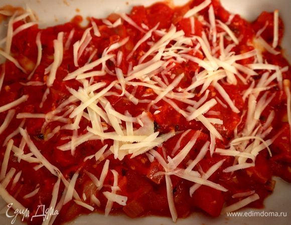 Духовку разогреть до 200°C. На дно огнеупорной формы поместить часть соуса, посыпать частью пармезана.