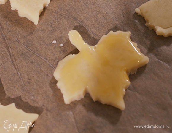 Кондитерскими формочками вырезать из теста фигурки, выложить на противень, застеленный бумагой для выпечки, и смазать яйцом. Выпекать печенье в разогретой духовке 15 минут.