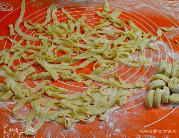 Затем тесто посыпаю мукой, складываю в 2–4 слоя и снова раскатываю, толщина теста должна составлять не более 2 мм. Сворачиваю пласты рулетиками и нарезаю полосками шириной не более 7 мм, поскольку в процессе варки полоски увеличиваются в 2 раза. Готовую лапшу разворачиваю и пересыпаю мукой.