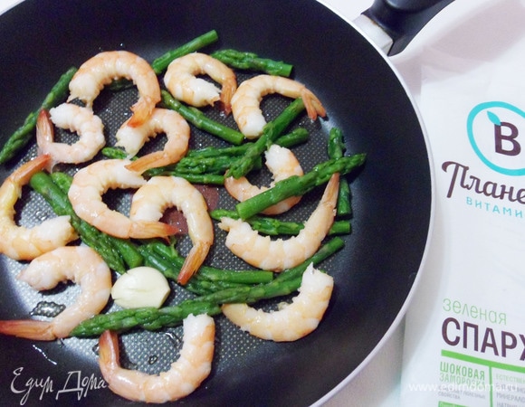 Разогреть на сковороде ложку оливкового масла, добавить зубчик чеснока и слегка его обжарить для ароматизации масла. Затем добавить креветки и оставшуюся горсть спаржи, обжаривать до готовности спаржи. Посолить.