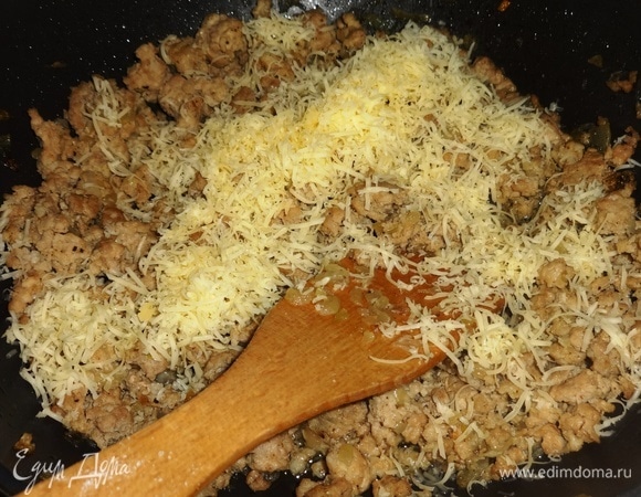 Добавить к обжаренному фаршу половину натертого сыра, перемешать.