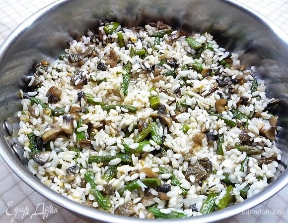 Через 5–7 минут после добавления первой партии бульона в рис, добавляем грибы и спаржу. Аккуратно перемешиваем и доводим до готовности в течение 15 минут, по необходимости добавляем бульон и пробуем рис на готовность.