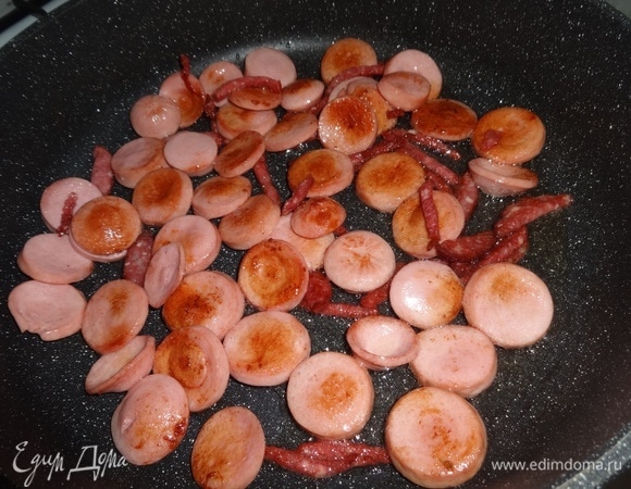 Нарезанные сосиски и колбасу выложить в разогретый жир от бекона и обжарить до румяности. Обжаренные продукты выложить в миску с беконом, оставляя жир в сковороде.