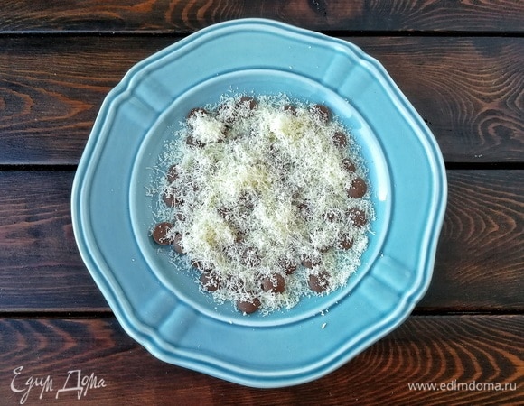 Тем временем начинаем сервировать. На дно каждой тарелки кладем по 20 г молочного шоколада. У меня кондитерский, я его не резала, он и так прекрасно растает. Если берете обычный, то нужно его мелко порубить ножом. Сверху шоколад посыпаем тоненьким слоем пармезана.