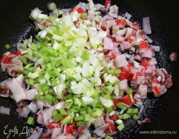 Обжариваем крабовые палочки в небольшом количестве растительного масла. Часть из них распустятся ленточками, а часть останутся кругляшками. Добавляем к обжаренным крабовым палочкам зеленый лук.