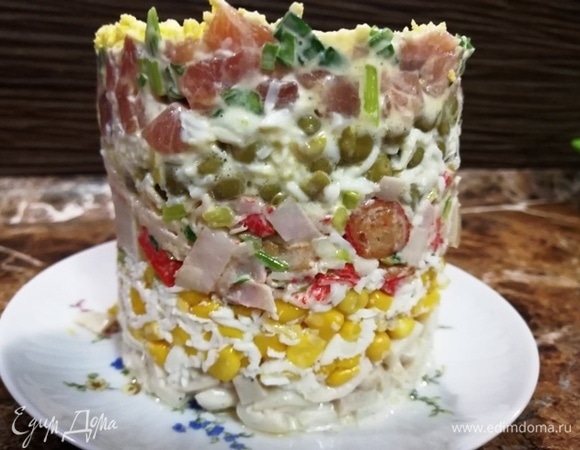 Выкладываем с помощью кулинарного кольца слоями кальмары, кукурузу, крабовые палочки, горошек, лосось. Украшаем верх салата тертым желтком.