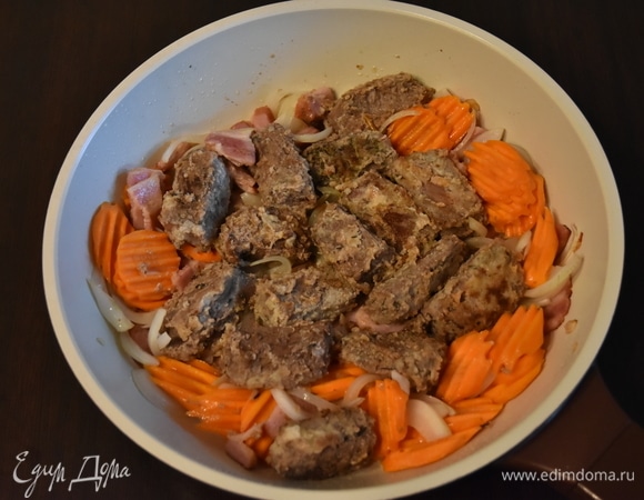 К бекону выложить крупнонарезанную морковь и лук. Обжарить в течение 5 минут и добавить мясо.