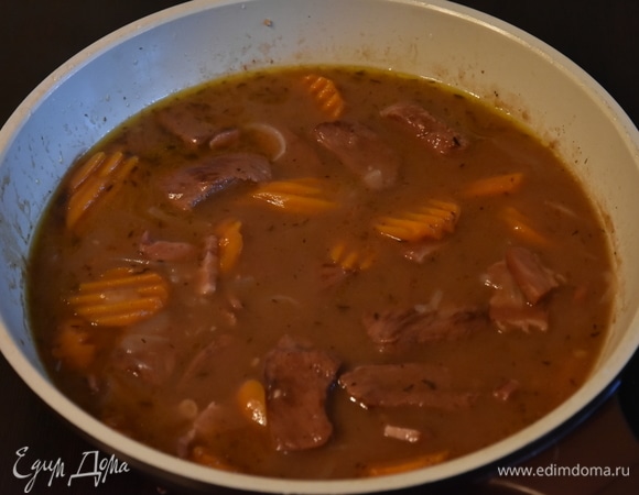 Влить бульон или воду, довести до кипения. Добавить вино. Накрыть сковороду крышкой, на медленном огне тушить блюдо часа 2. За 30 минут до готовности блюдо посолить и поперчить по вкусу. Добавить крупнонарезанные грибы. В процессе тушения соус загустеет, а мясо станет очень мягким. Подавать, посыпав зеленью.