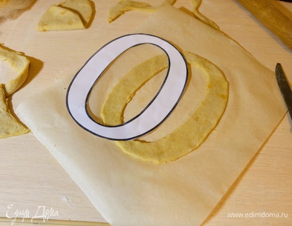 Раскатываем тесто толщиной 3–5 мм, перекладываем на пергамент и вырезаем буквы по заранее распечатанному шаблону. Коржи пекутся быстро — 5–7 минут.