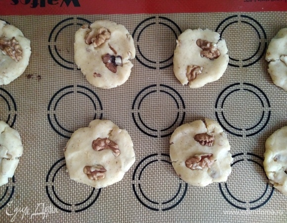 Духовку разогреть до 180°C. Приготовить бумагу для выпечки или силиконовый коврик. Из теста скатать шарики, приплюснуть немного. Распределить на небольшом расстоянии друг от друга. Сверху украсить целыми орешками.