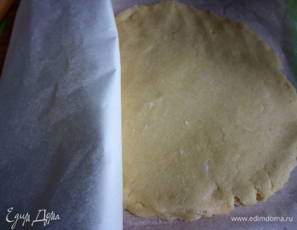 Духовку разогреть до 180°C. Тесто немного раскатать, положить на лист пергаментной бумаги, накрыть другим листом пергамента.