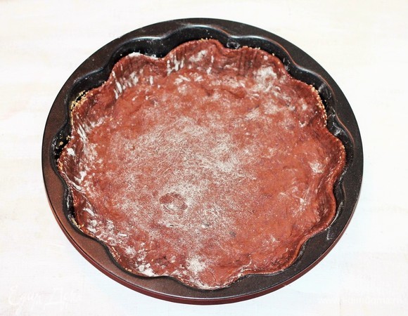 Форму для выпечки диаметром 24 см застелить пергаментом, смазать маслом и посыпать панировочными сухарями или мукой. Одну часть теста раскатать в круг при помощи посыпанной мукой скалки, перенести в формочку, вылепить бортики, наколоть дно вилкой.