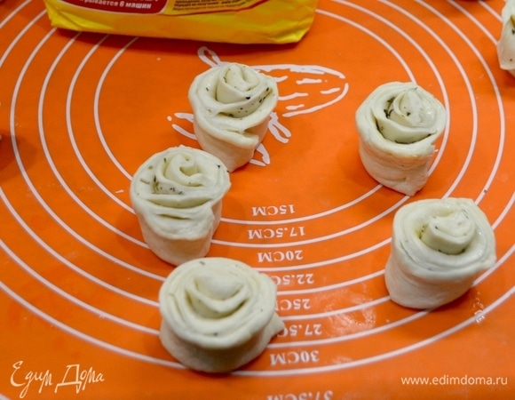 Далее тесто делим на несколько кусков и из них тонко раскатываем листы, смазываем растопленным сливочным маслом. Посыпать, если есть, ореховой травой (у меня любимые прованские травы). Сворачиваем пласт теста в рулет. Готовые рулеты режем на кусочки размером 3 см и формируем розочки.