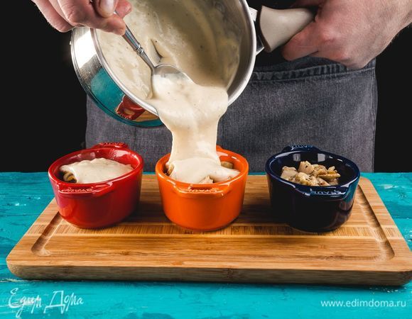 В кокотницы выложите курицу с грибами и чесноком, добавьте соус бешамель.