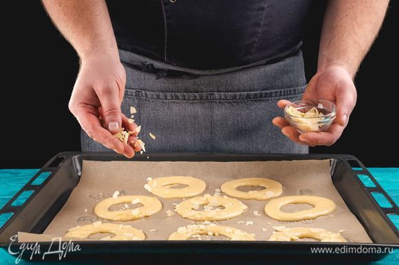 Противень застелите пекарской бумагой, выложите тесто в кондитерский шприц и сформируйте основу для пирожных, выдавливая тесто в форме колец. Сверху посыпьте заготовки по кругу миндальными лепестками. Поместите противень с пирожными в разогретую духовку и, понизив температуру до 180°С, выпекайте 15 минут, затем уменьшите температуру до 170°С и выпекайте еще 15 минут. Затем выключите духовку и оставьте пирожные еще на 5–7 минут в духовке.