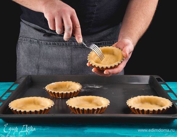 Через полчаса достаньте тесто из холодильника, разделите на порции, раскатайте и выложите в формочки для тарталеток. Наколите немного вилкой дно каждой тарталетки. Поставьте заготовки в морозилку на 10 минут. Тем временем разогрейте духовку до 250°С. Достаньте из морозилки заготовки и поставьте их на противне в духовку. Выпекайте 20 минут до румяного цвета. Готовые тарталетки достаньте из духовки и немного остудите.<br />
 